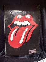 Photograph of the full poster showing the tongue and lips logo with "The Rolling Stones" text on a black background, mounted on a board, with visible surface wear.