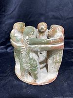 Side view of terra-cotta candle holder showing four embracing figures with aged patina