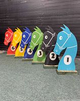 Six numbered wooden horse head race markers with painted bright colors in a row, view from side angle