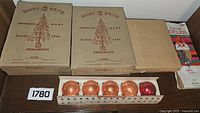 Two original Shiny Brite cardboard boxes, a plain cardboard box, and one open box of orange and red ball ornaments on a table.