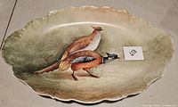 Top view of the oval Limoges porcelain platter featuring two painted pheasants on a naturalistic background with scalloped edges and gold trim.