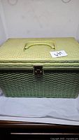 Closed green woven look plastic sewing box with handle and metal clasp front view