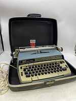 Full view of Smith-Corona Electra 120 electric typewriter inside open black hard case with attached power cord.