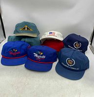 Overview photo showing all 10 vintage snapback hats arranged in rows, featuring Raybestos, Colonial Cadillac, American flag, and other logos with rope brims and embroidered branding.