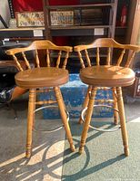 Pair of vintage wooden swivel bar stools with spindle backs, wooden seats, and metal footrests under bright indoor lighting.