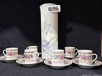 Photo showing the set of six floral teacups with saucers alongside the tall Kaiser vase featuring iris flowers.