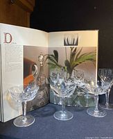 Three Waterford Dunloe pattern champagne glasses in front of a Waterford collector guide book open to a page showing similar glassware.