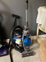 Both vacuum cleaners together: Bissell upright in front, Mastervac shop vac behind with hose coiled.