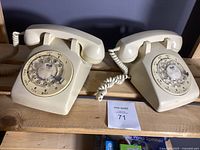 Two vintage rotary dial telephones placed side by side on wooden shelves, showing overall condition and design.