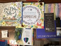 Overview of all items: two adult colouring books, Staedtler coloured pencils pack, Fabriano watercolor paper pad, charcoal pencils, and a sale tag.