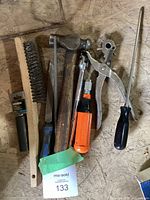 Full set of assorted hand tools on wooden surface showing hammer, screwdriver, ratchet, wire brush, metal file, leather punch, and additional socket