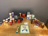 Wide view of all vintage Avon fragrance and cosmetic boxed items on wooden table against gray wall.