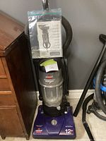 Front view of Bissell PowerForce 6579-3 vacuum cleaner showing clear dust container, model label, and attached operator's manual in plastic bag.