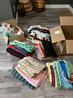 Photo showing a variety of fabric pieces laid out on floor with some in open boxes, including patchwork, solid colors, and patterned fabrics.