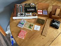 Overview of all items including decks of cards, cribbage boards, storage boxes, and travel checkers set on wooden table