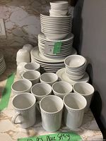Wide view of stacked white porcelain dinnerware showing mugs, plates, bowls, and smaller dishes with embossed dot border detail.