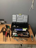 Photo showing the open toolbox with some tools placed on the table next to it including screwdrivers, pliers, wrenches, and cutters.