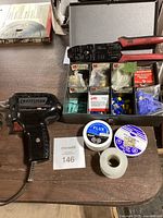 Full view of the soldering tool, wire stripper, various electrical connectors in packages, rolls of wire, flux jar, and spool of solder wire on a wooden surface.