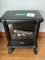 Front view of black electric heater stove with faux logs visible through glass panel.