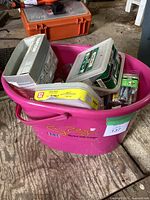 Top view of pink plastic bucket filled with various hardware containers and packs including plastic boxes and metal tin inside bucket.