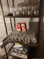 Shelf with multiple clear glass canning jars of various sizes and designs, some with visible wear, plus unopened Bernardin snap lid boxes.