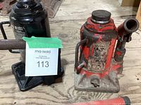Red hydraulic bottle jack and black hydraulic bottle jack positioned side by side on wooden surface showing overall condition and wear.