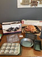 Cookware set and roasting pan boxed shown with baking pans and muffin tray arranged in front