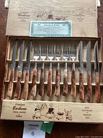 Full view of all 12 utensils laid in wooden box, showing 6 steak knives and 6 forks with faux horn handles.