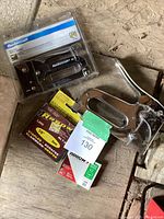 Mastercraft T-50 staple gun in packaging, manual metal staple gun, and two boxes of staples on wooden surface.