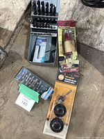 Photo showing metal case with Mastercraft drill bit set including multiple sizes of twist drill bits, sealed pack of drill bits, original packaging of Drive90 right-angle drive attachment, and Milescraft hole saw kit in packaging.