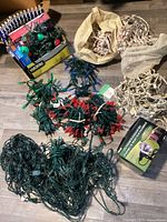 Photo showing multiple tangled and bundled strings of Christmas lights in red, green, and white wiring, plus a cardboard box with more lights and a net light.