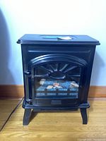 Front view of the electric stove heater showing its black finish, stove-like design, and glass door with faux logs inside.