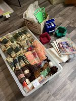 Wide angle photo of entire craft kit including yarn skeins, plastic canvas sheets, two small plastic canvas chairs, and instruction booklets all contained in a clear plastic bin.
