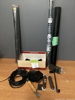 Front view of screen replacement kit items including mesh rolls, spline roll, corner clips, and hand tools laid on a table against wall