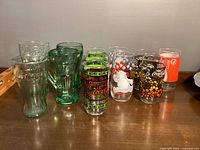 Full view of all 11 Coca-Cola glasses on wooden surface showing color and design variety