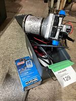 Photo of Shurflo water pump sitting inside a toolbox with cables and a Coleman solar charge controller box next to it.