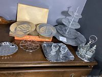 Photo showing full lot including three-tiered serving tray, two aluminum steak platters on wooden boards, large round platter, square serving tray with glass containers and spoon, and metal condiment set with glass bottles and shakers.