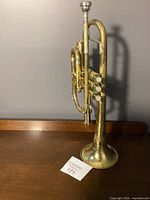 Vintage brass trumpet standing upright on a wooden surface showing the side valve cluster and mouthpiece attached.