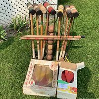 Front view on grass showing wooden croquet mallets, balls in wicket frame, stake across front and two lawn darts boxes