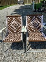 Front view of both vintage patio chairs side by side showing the brown and white woven geometric pattern seats and backs, metal frames, and plastic armrests.