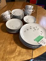Wide shot of entire vintage porcelain dinnerware set including 6 dinner plates, 7 small plates, 4 small saucers, and 9 cups stacked on wooden table.