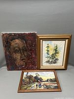 Group of three paintings including a textured portrait and two framed landscapes seen from front