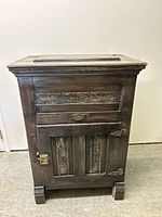 Full view of wooden antique ice box refrigerator showing carved details on front and metal latch hardware