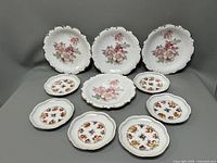 Full view of all 10 plates arranged showing two types of plates: larger scalloped with floral center and smaller pierced edge floral plates.
