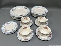 Photo showing stacked dinnerware including plates, cups, and saucers with a floral pattern and blue decorative border.