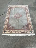 Full view of rectangular hand woven Chinese art deco medallion rug with light greenish-gray field, central medallion, and detailed border on concrete.