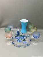 Overview showing all ten colored art glass items arranged against neutral backdrop including vase, goblets, paperweights, and decorative platter.