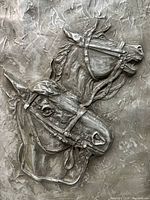 Close-up of two horse heads in high relief composite sculpture showing bridle details and textured background.