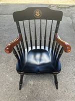 Front view showing the spindle back and the emblem on the upper backrest, natural wood armrests and black seat.