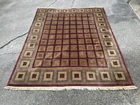 Full view of hand woven wool rug on outdoor concrete surface showing geometric square pattern and fringe.